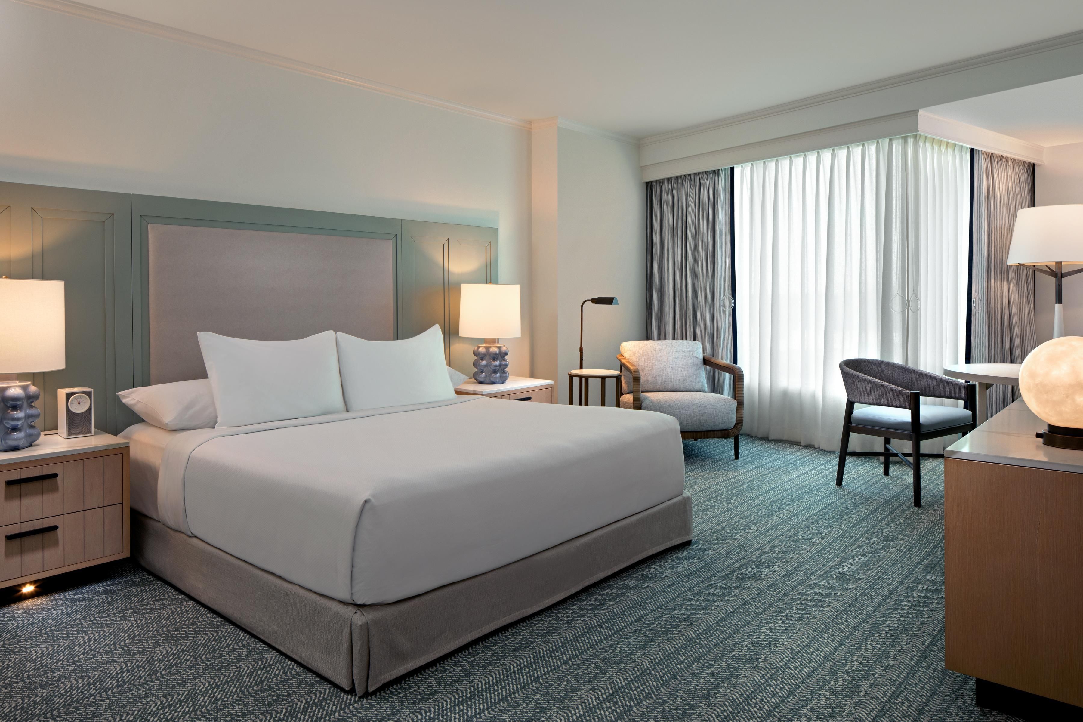 A hotel room with a large bed, two bedside tables, a desk, a chair, and a lamp.