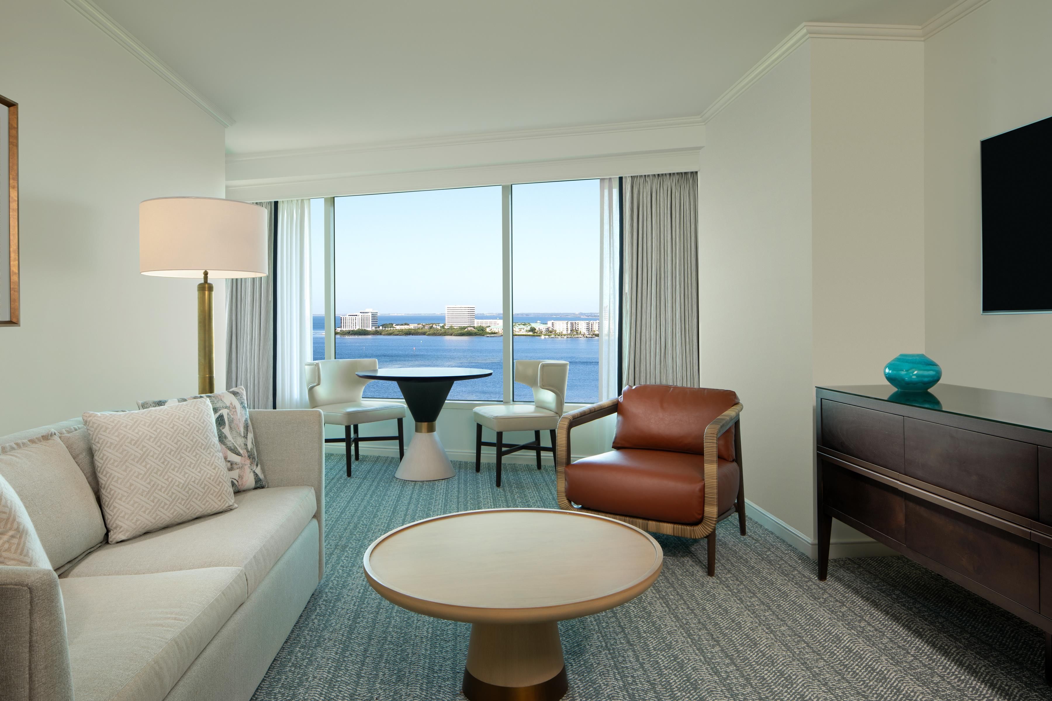 Habitación de hotel con sofá, sillón, mesa de comedor y vista al mar.
