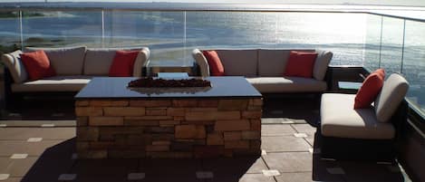 Une terrasse avec une table basse en pierre, deux canapés avec des coussins rouges et une vue sur la mer.