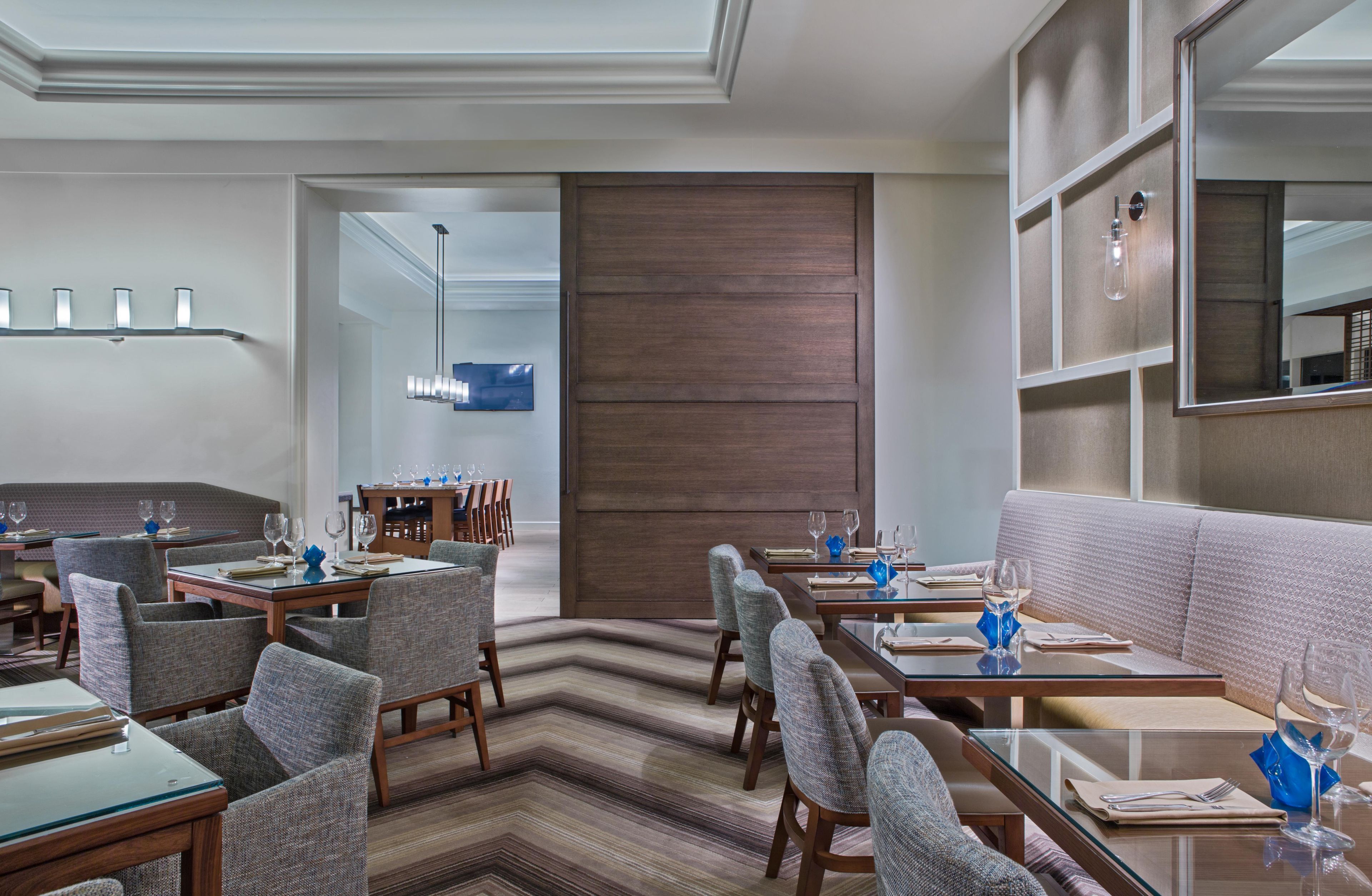 A modern dining area with multiple tables and chairs, a sofa, and a large mirror.