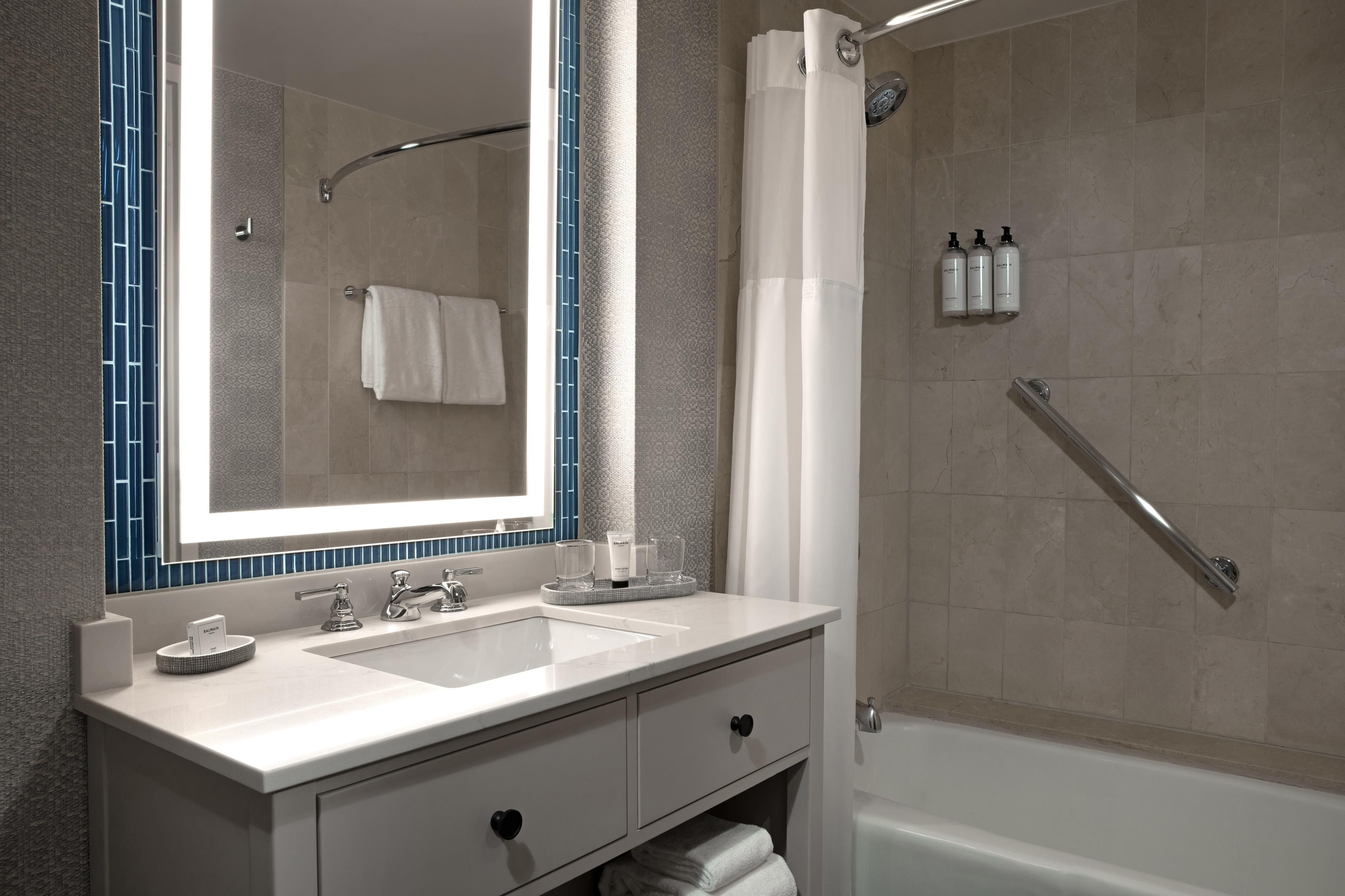 A modern bathroom with a large mirror, two sinks, a bathtub, and a shower.