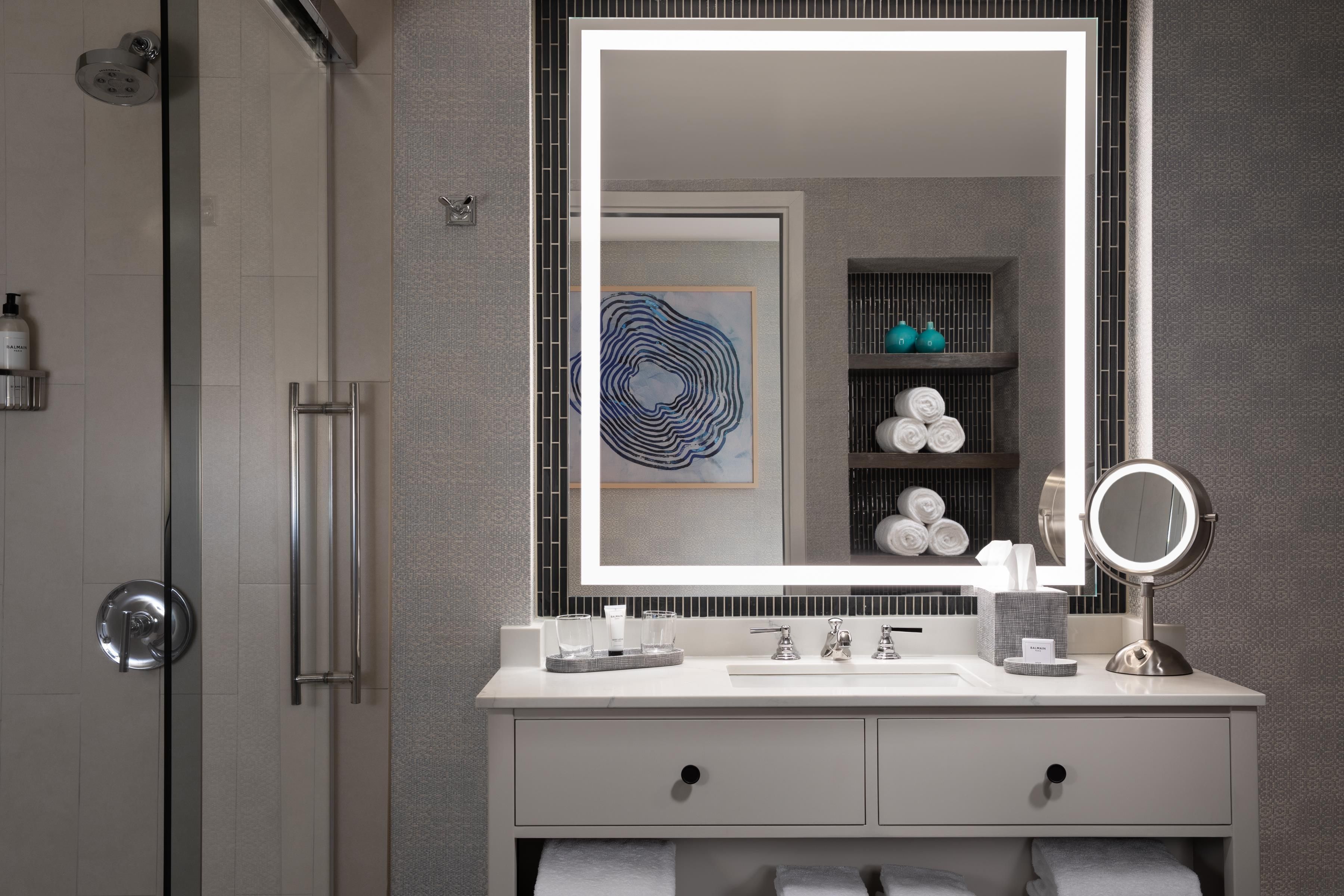 A modern bathroom with a large mirror, a shower, and a vanity with toiletries.