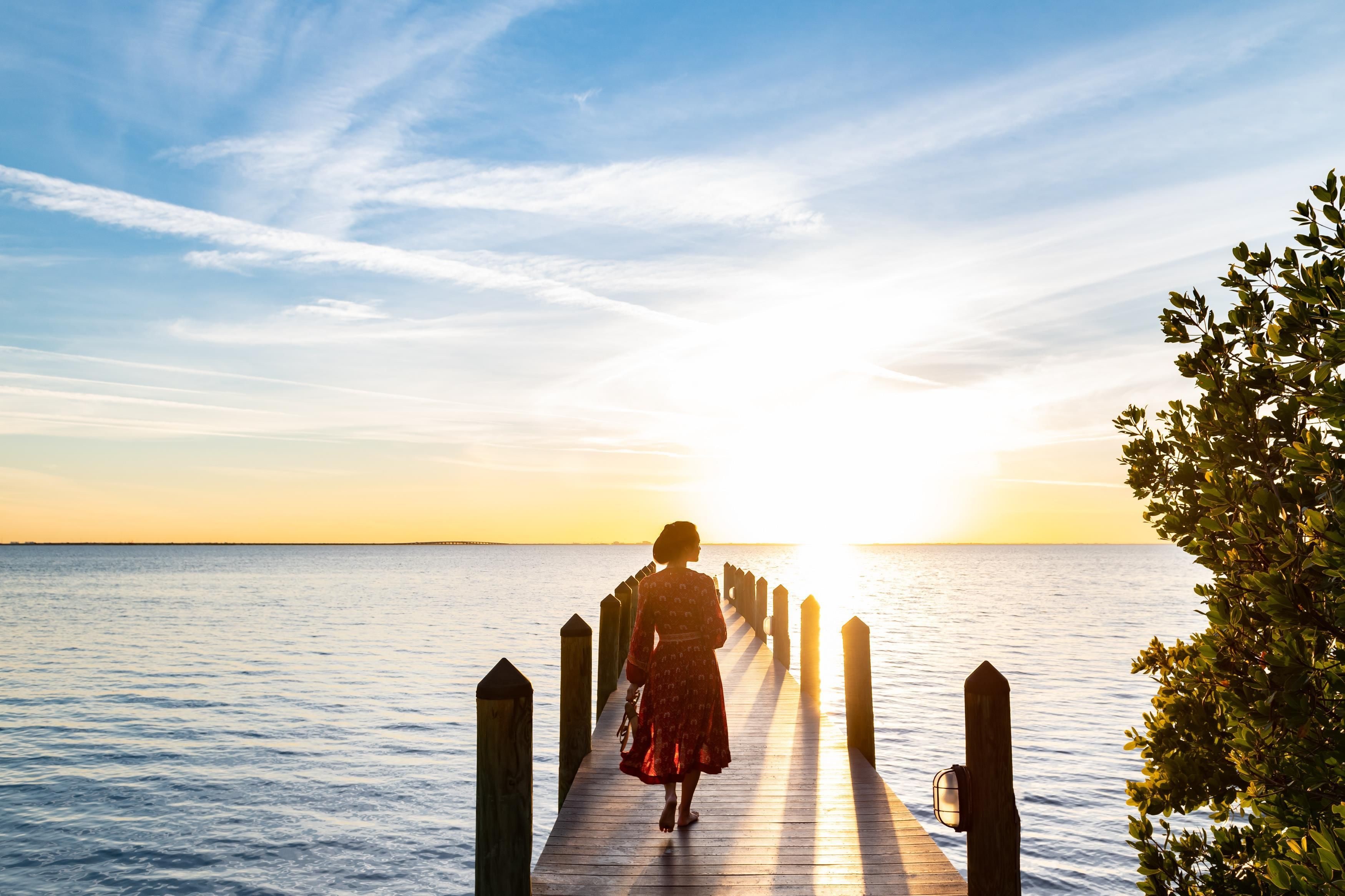 A wooden pier extending into calm water with a sunset in the background.
