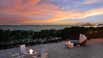 Relax on the beach with comfortable seating and a warm fire pit, surrounded by a serene ocean view.