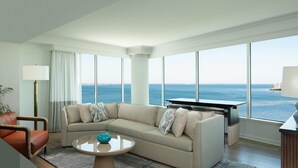 Un salon moderne doté d’une grande fenêtre donnant sur la mer, d’un canapé beige, d’une table basse ronde et d’un meuble pour la télévision.