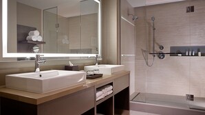 Un baño moderno con dos lavamanos, un espejo grande y cabina de ducha con mampara de vidrio.