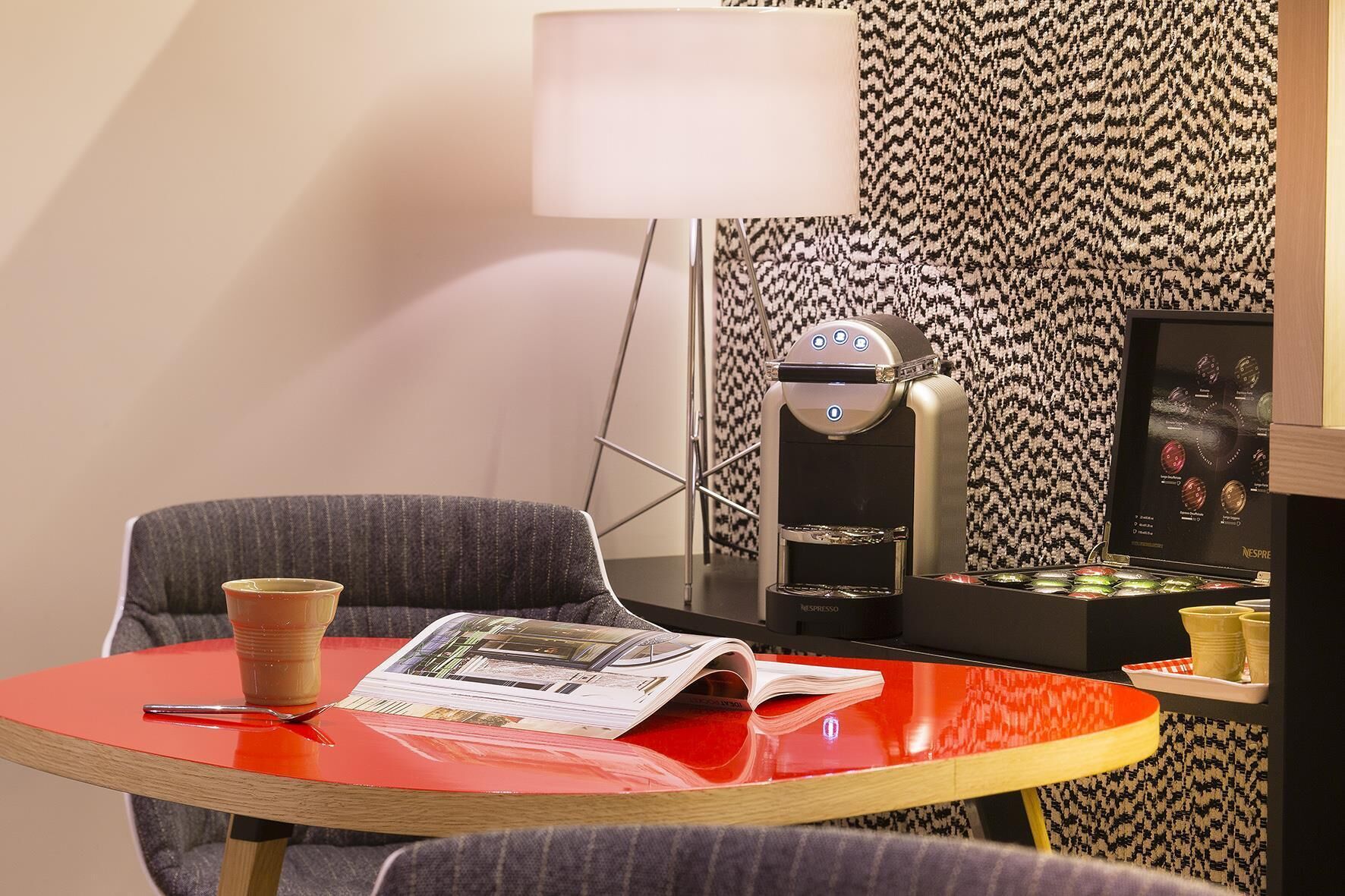 A room with a red table, a grey chair, a coffee machine, and a magazine.