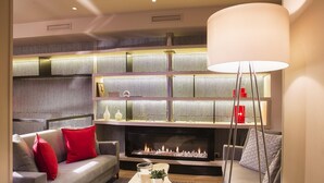 A modern living room with a fireplace, a sofa with red cushions, a coffee table with decorative items, and a large floor lamp. - Best Western Quartier Latin Pantheon (Paris)