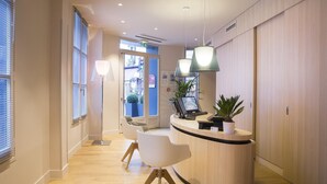 A reception area with a curved wooden desk, two white chairs, a floor lamp, and a potted plant. - Best Western Quartier Latin Pantheon (Paris)