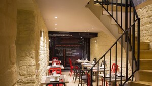 A restaurant with a stone wall and a staircase leading to an upper level. Tables are set with red chairs and white tablecloths. - Best Western Quartier Latin Pantheon (Paris)