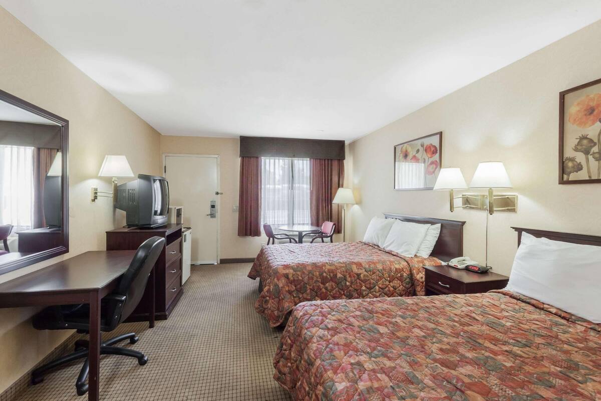 A hotel room with two beds, a desk, a television, a chair, and a window with curtains.