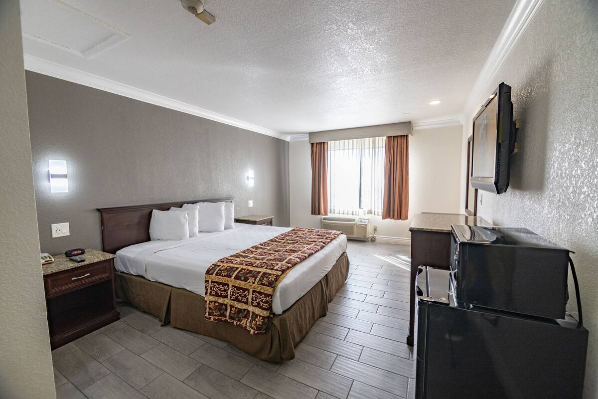 A hotel room with a bed, a desk, a TV, and a window with curtains.
