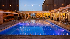 An outdoor swimming pool with a wooden deck, surrounded by buildings with large windows and string lights. - Delamar Traverse City (Traverse City)