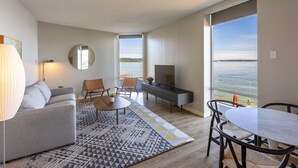 A modern living room with a sofa, coffee table, TV, and dining area. - Delamar Traverse City (Traverse City)