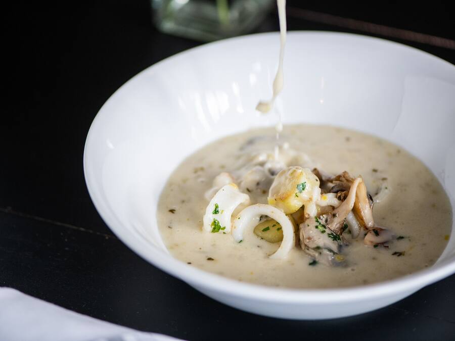 A bowl of creamy soup with chunks of chicken and vegetables, being poured into it.