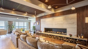 A modern living room with a fireplace, sofas, and a large window overlooking the sea. - Delamar Traverse City (Traverse City)