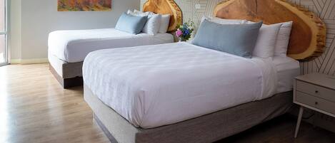 A modern bedroom with two beds, a wooden headboard, a geometric wall pattern, and a wooden floor.