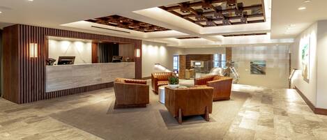 A spacious lobby with a reception desk, leather seating, and a modern ceiling design.