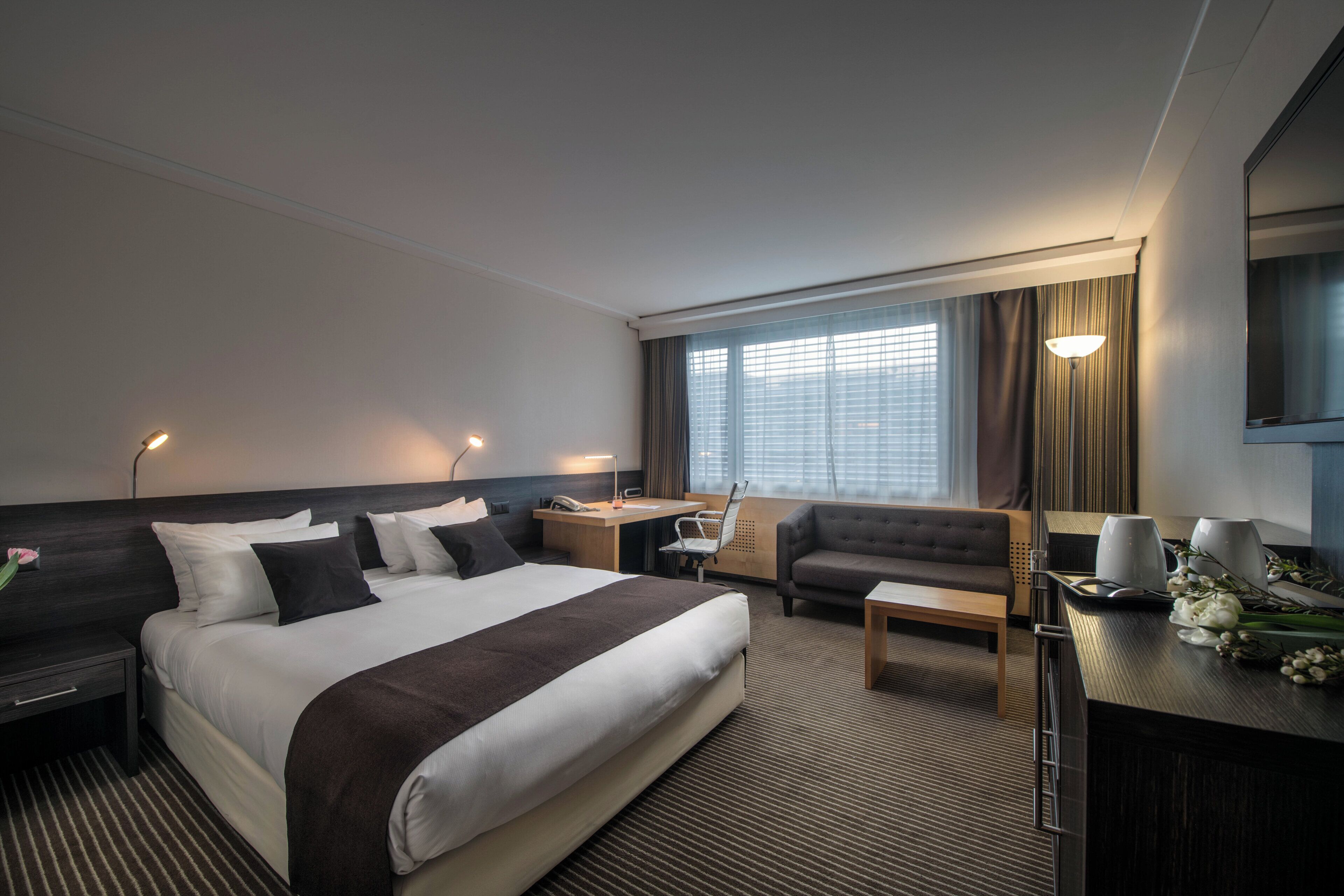 A hotel room with a large bed, a sofa, a desk, and a chair.
