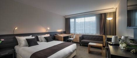 A hotel room with a large bed, a sofa, a desk, and a chair.