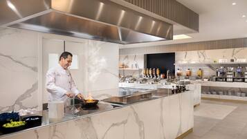 A modern kitchen with a chef preparing food, marble countertops, and a buffet area with various dishes and condiments.