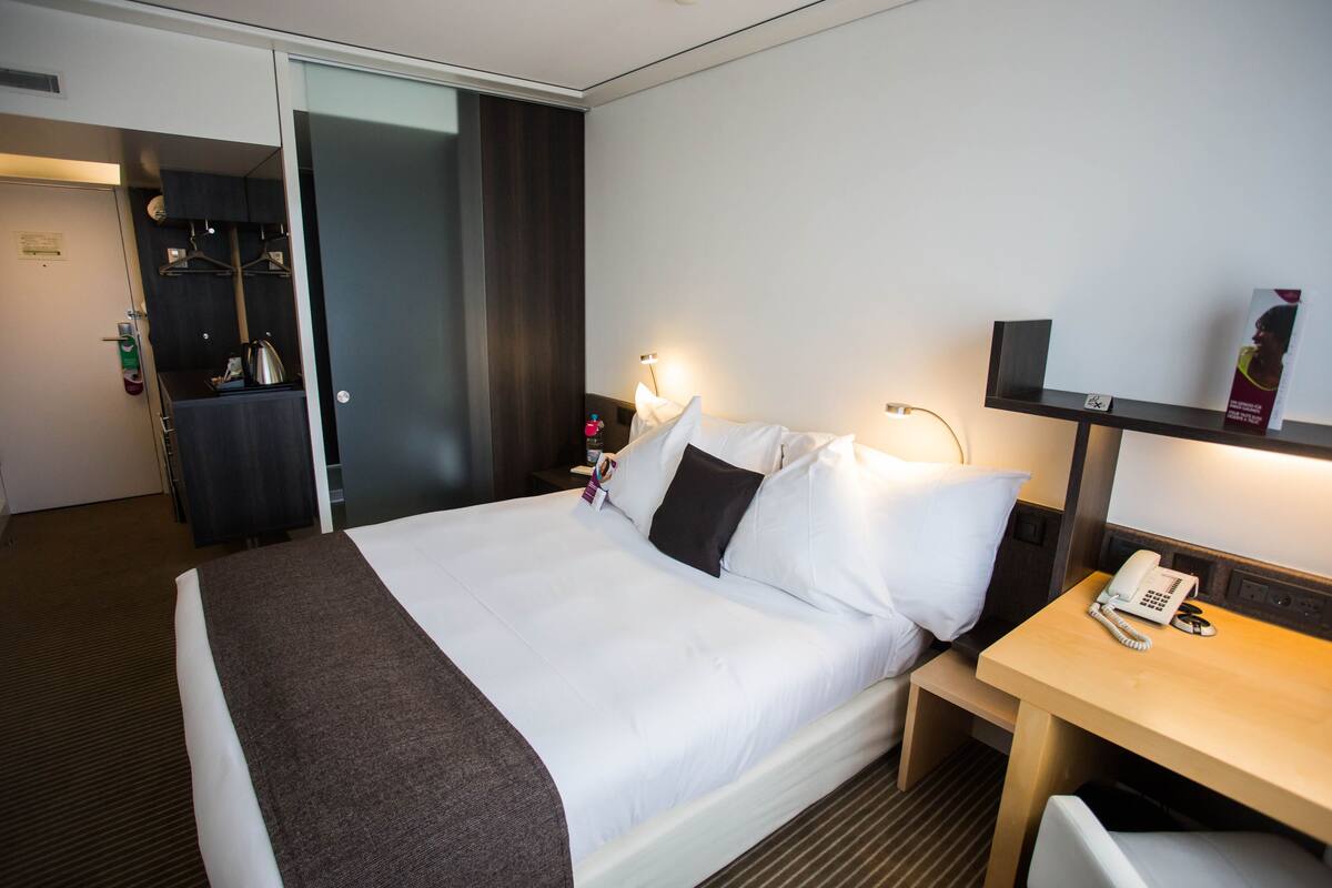 Una habitación de hotel con cama, mesita de noche y escritorio con teléfono.
