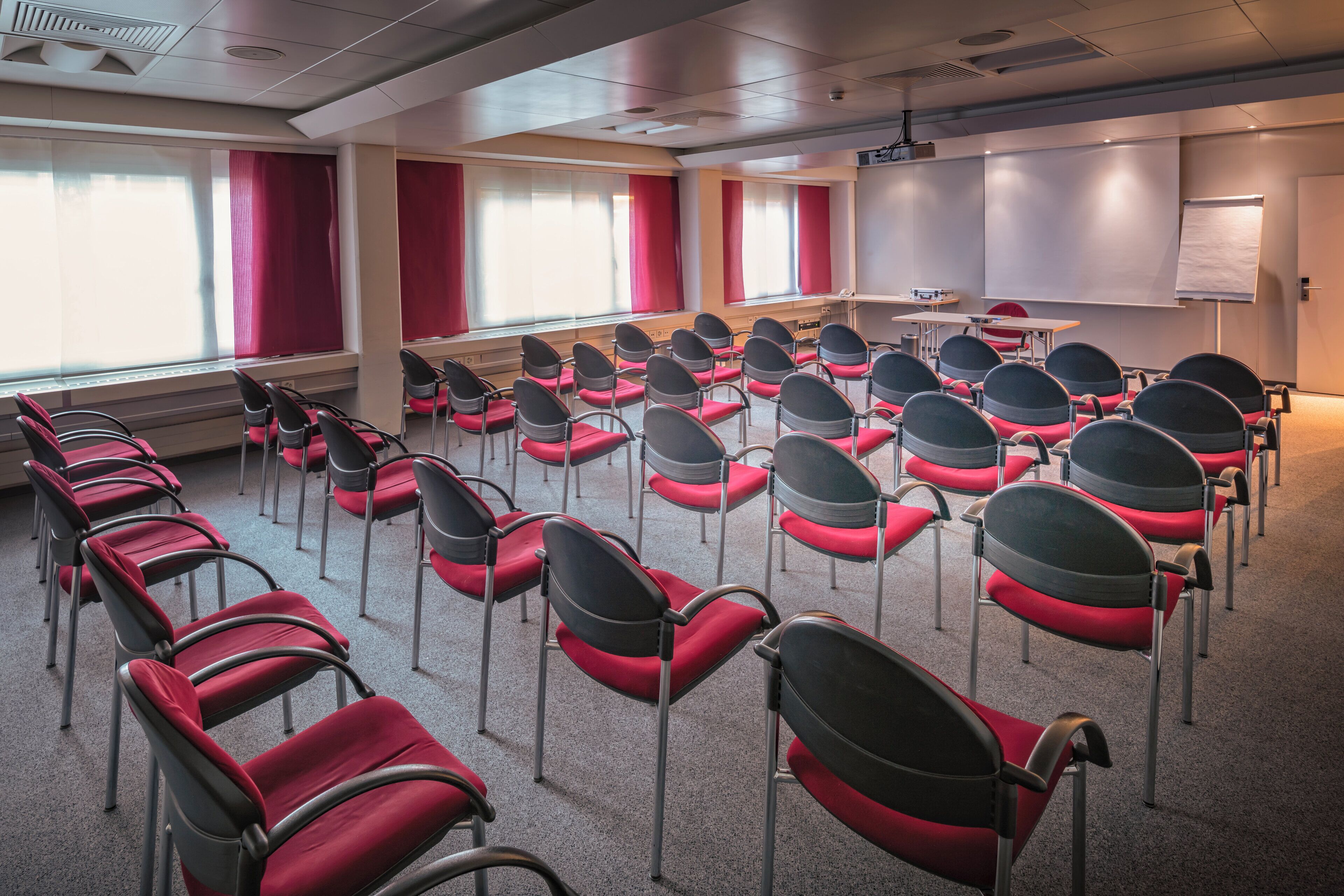 Een vergaderzaal met rijen stoelen, een projectiescherm en een whiteboard.