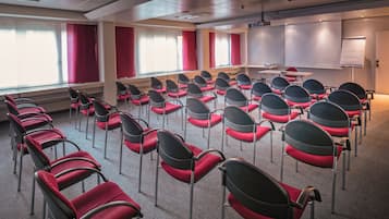 Een vergaderzaal met rijen stoelen, een projectiescherm en een whiteboard.