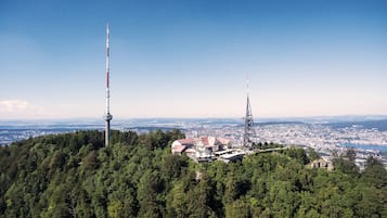 A mountain-top hotel with a tower, surrounded by dense forest, offering panoramic city views.