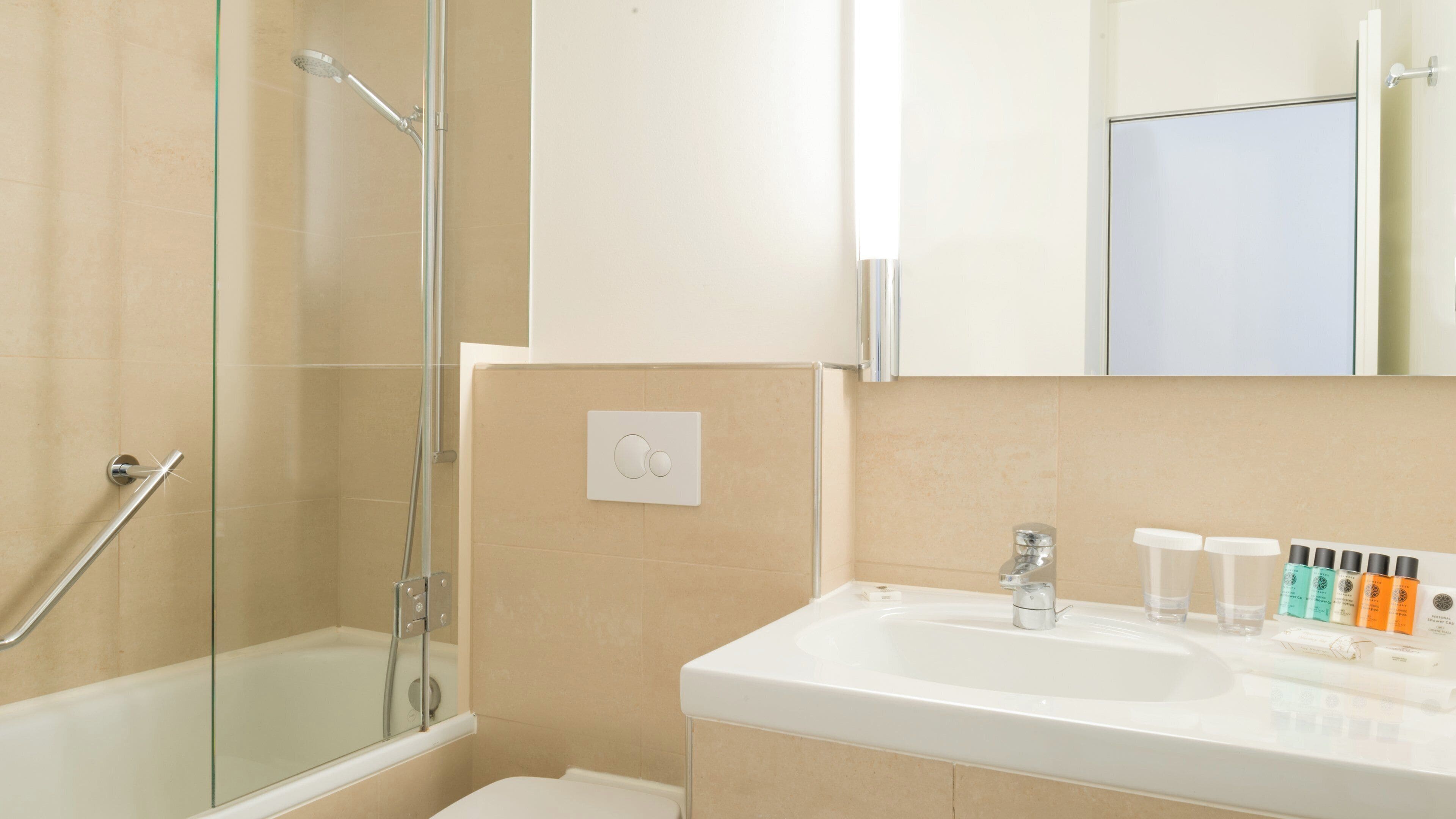A bathroom with a glass-enclosed shower, a white sink with toiletries, and a mirror above the sink.