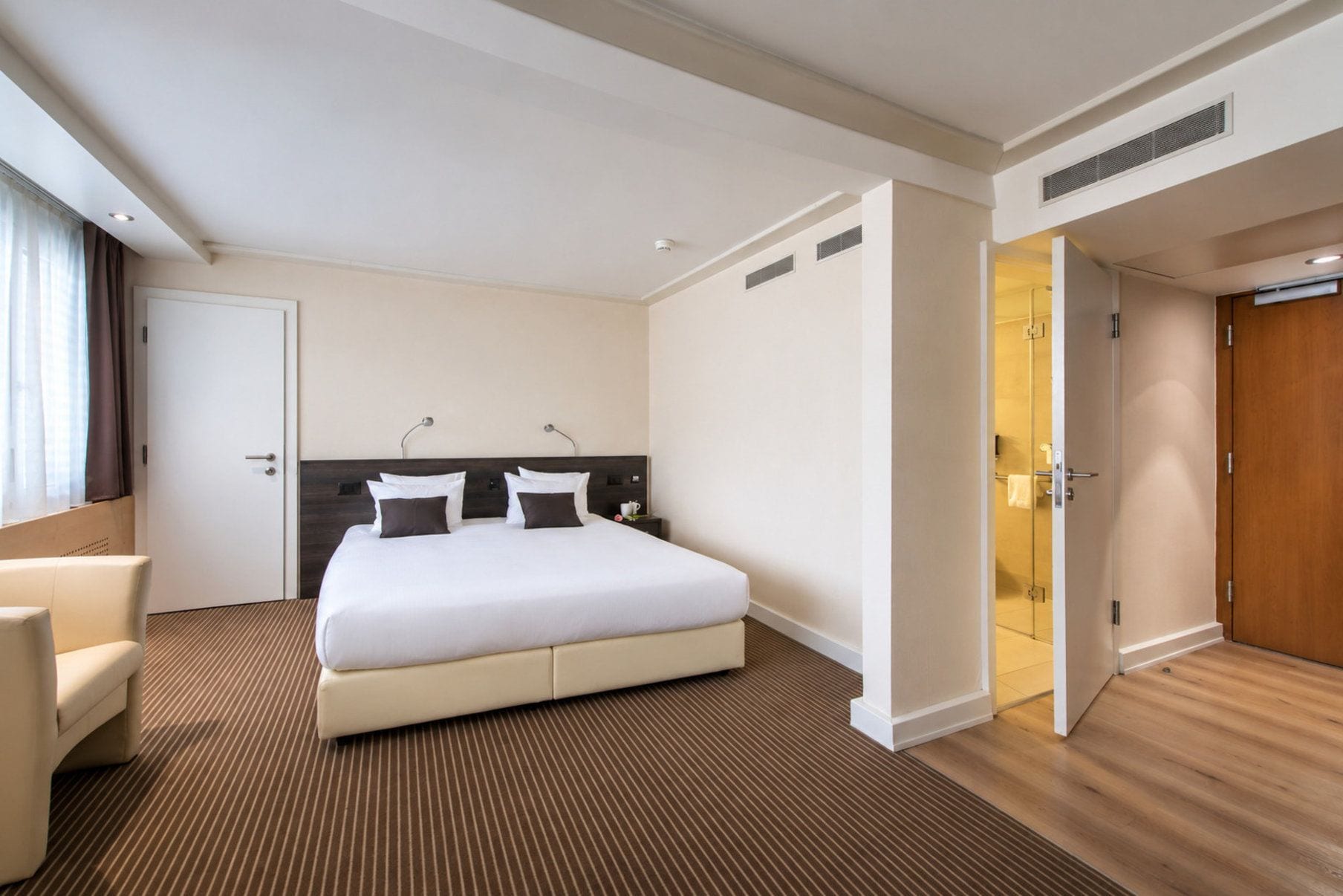 A hotel room with a large bed, a bedside table, a chair, and a bathroom door.