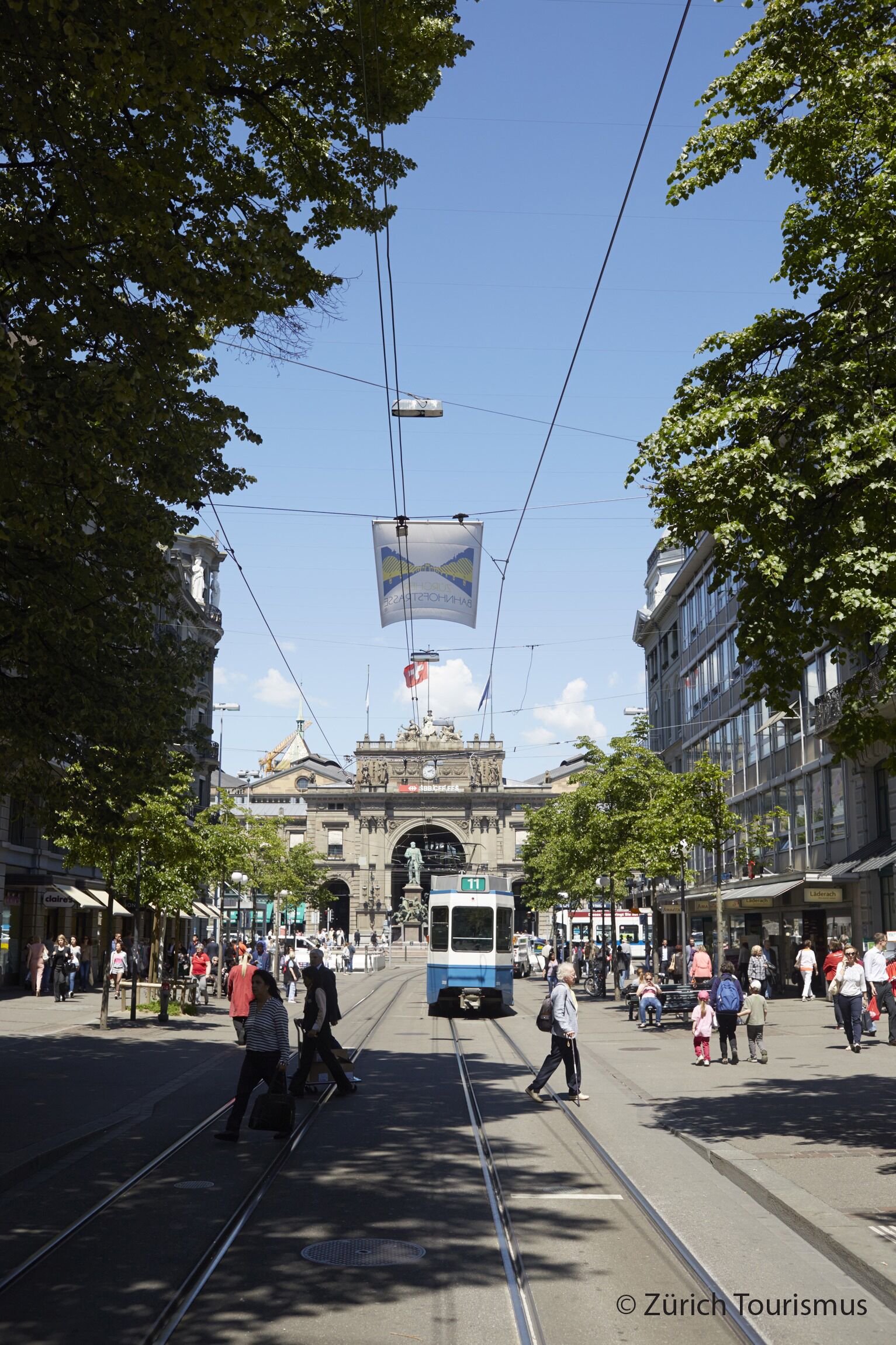 A tram moving through a busy urban street with pedestrians and buildings.