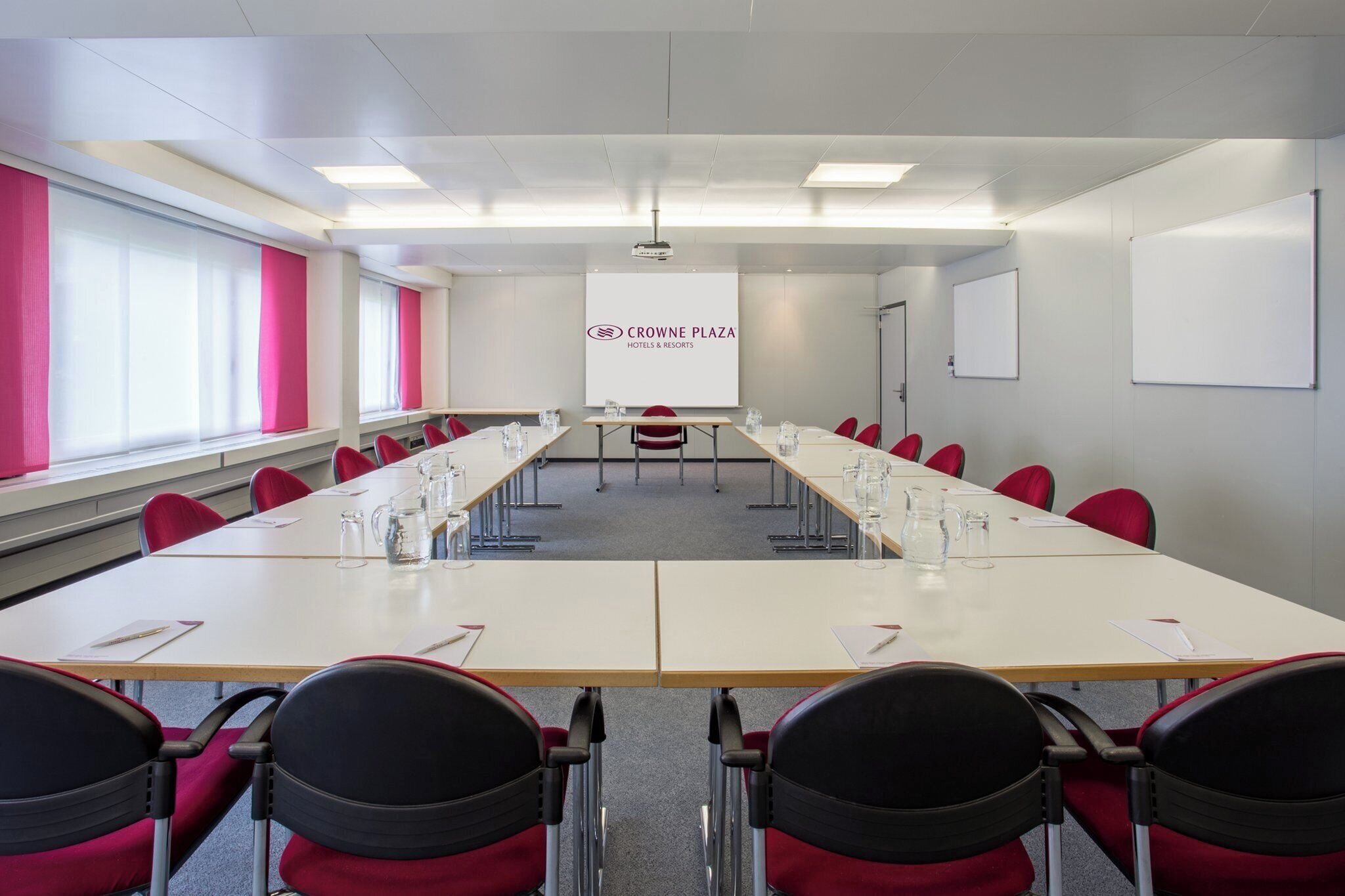 A conference room with a long table, red chairs, a projector screen, and a whiteboard.