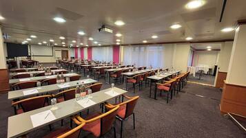A conference room with multiple tables and chairs, equipped with water bottles and papers, and a projector mounted on the ceiling.