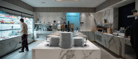 Cocina moderna con encimeras de mármol, una isla central con platos apilados y un refrigerador con frutas.