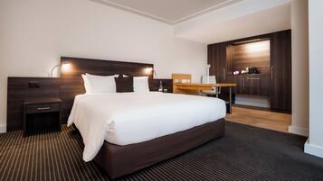 A hotel room with a large bed, a desk, a chair, a nightstand, and a wardrobe.