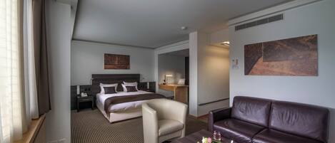 Habitación de hotel con cama, escritorio, sofá de cuero y mesa de centro con una bandeja de tazas y flores.