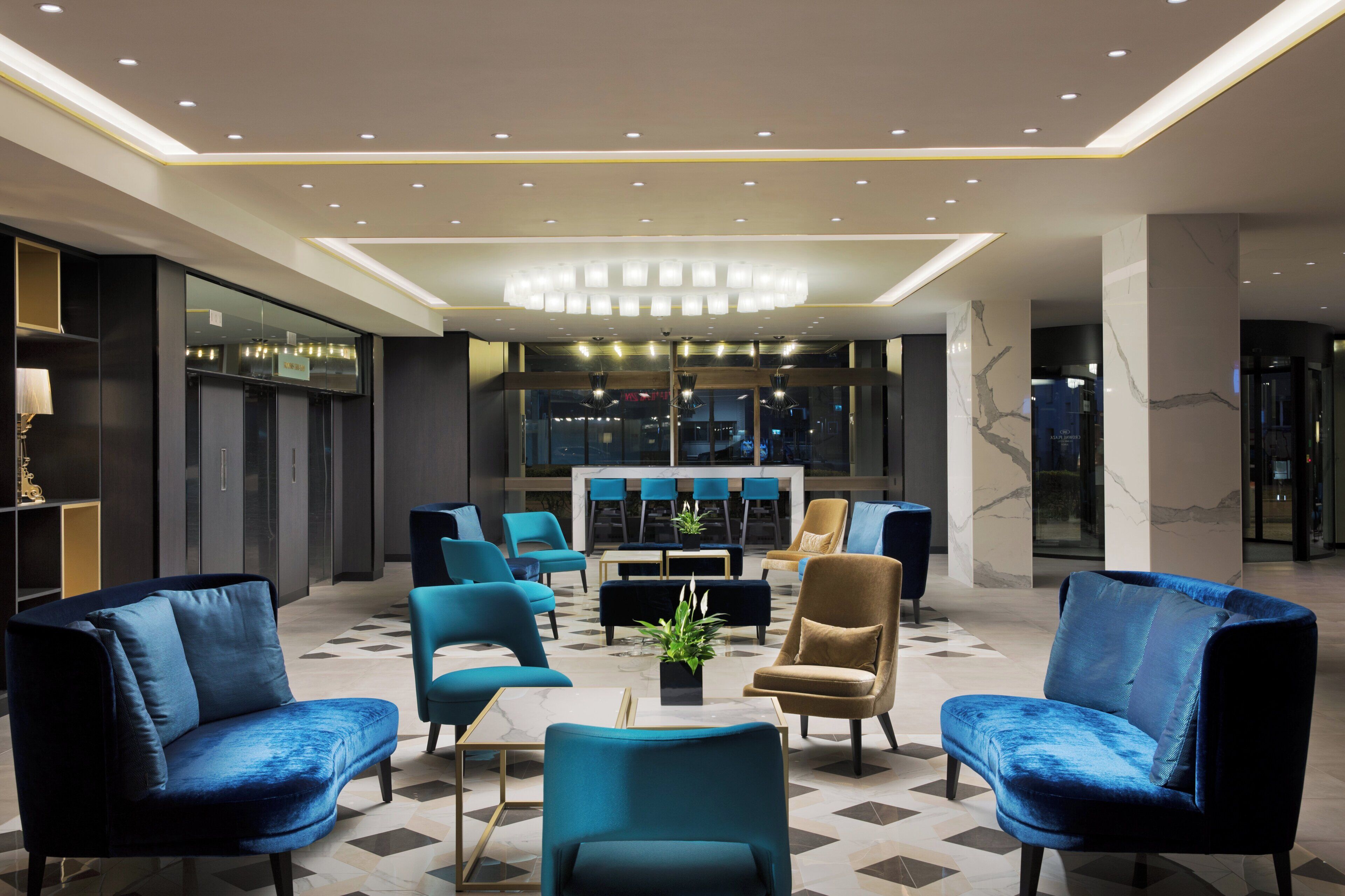 A modern lobby with a central seating area, a bar, and a view of the cityscape through large windows.