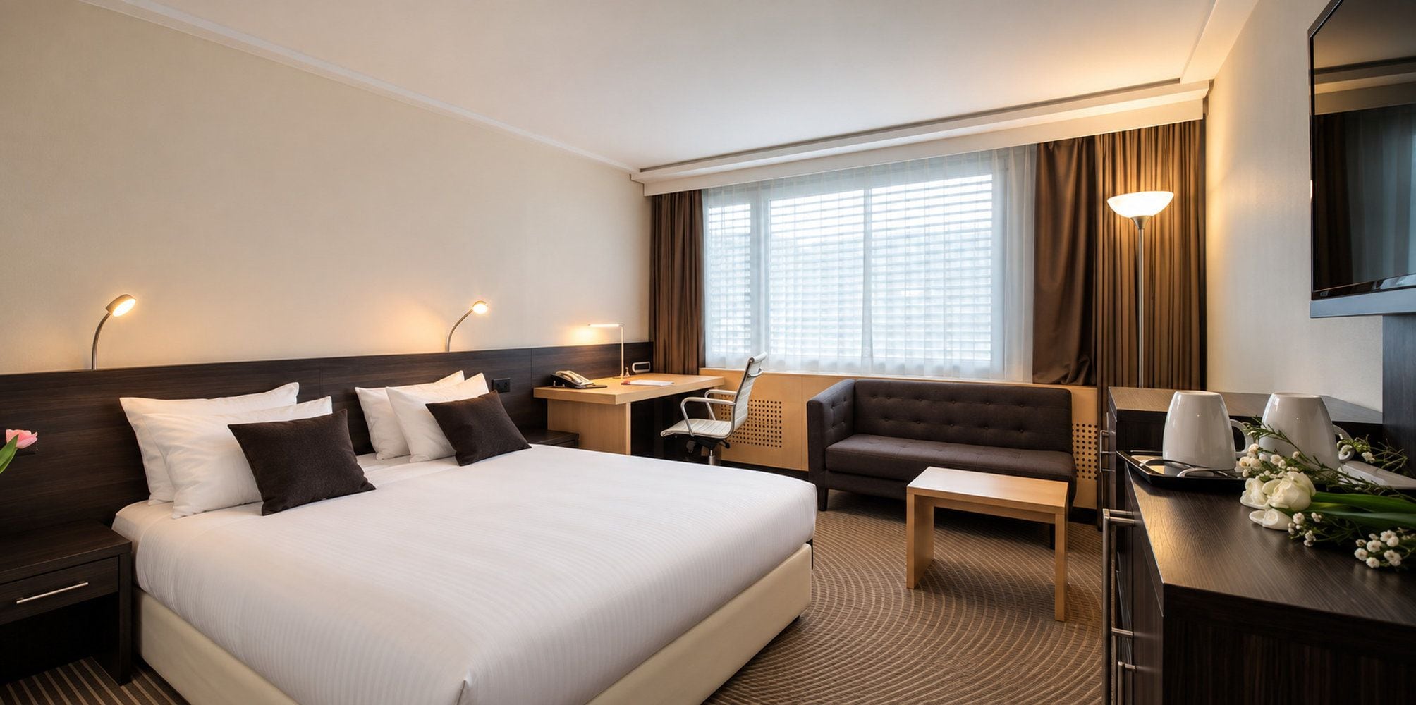 A hotel room with a large bed, a desk, a sofa, and a TV.