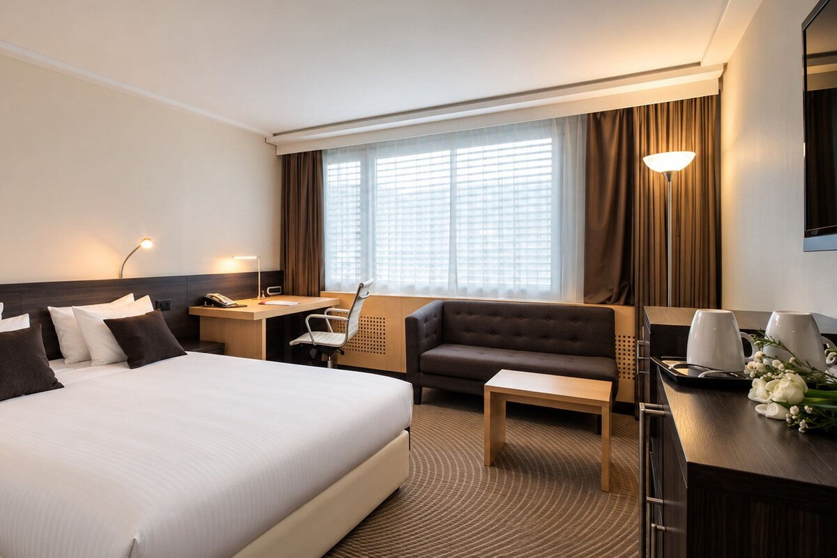 A hotel room with a large bed, a desk, a sofa, and a TV.