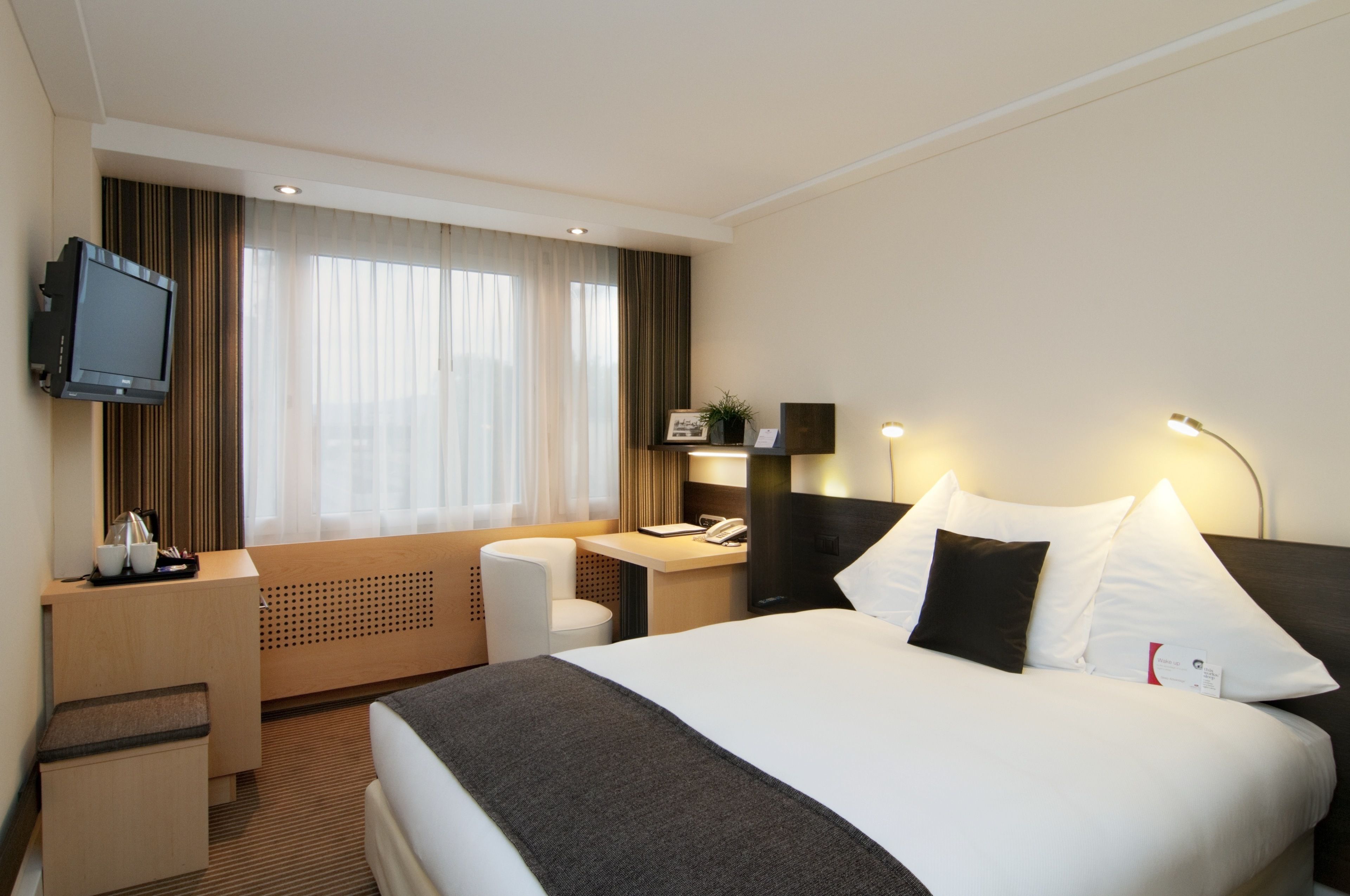 A hotel room with a large bed, a desk, a chair, a television, and a window with curtains.