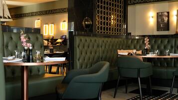 A restaurant interior with a green upholstered booth seating area, tables with chairs, and a decorative wall with a geometric pattern.