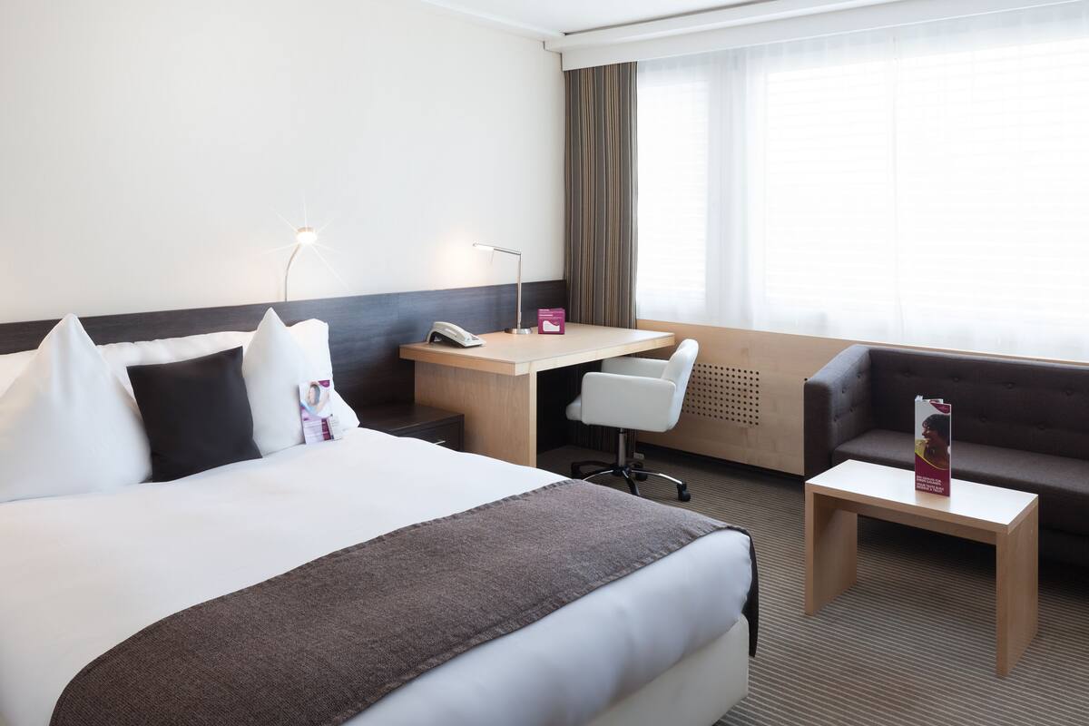 Una habitación de hotel con una cama grande, un escritorio, una silla y un sofá.