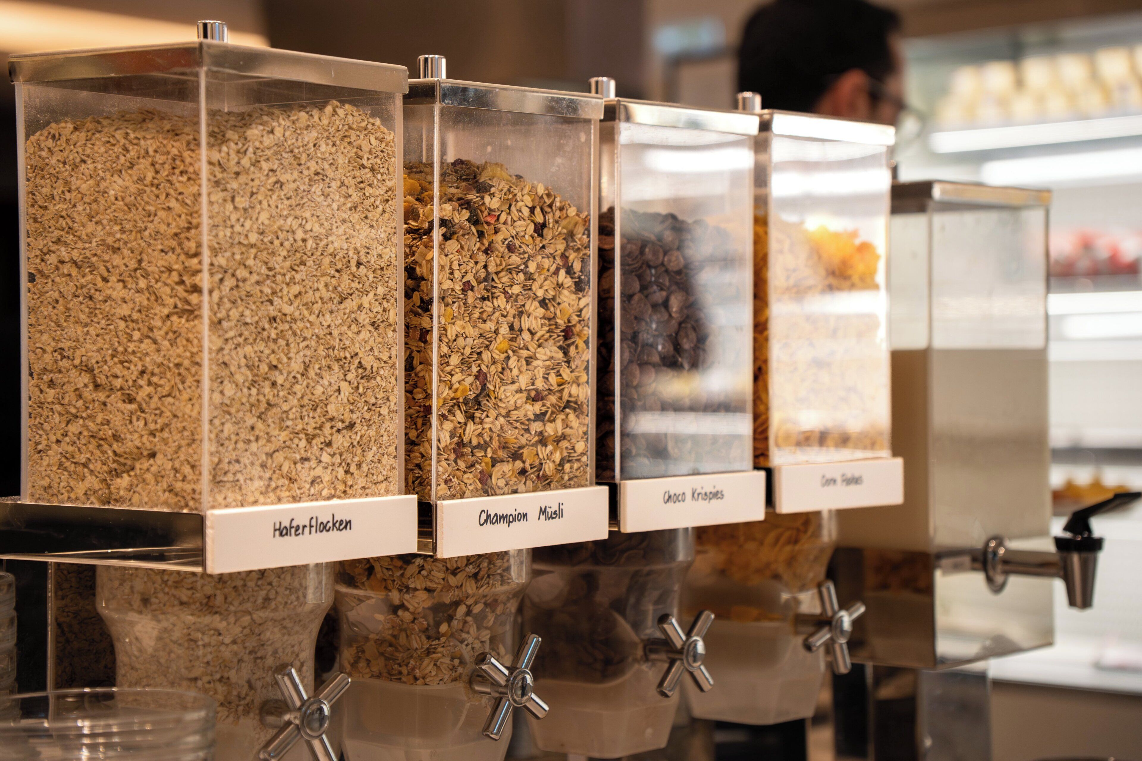 A food dispensing station with labeled containers for different types of cereal.
