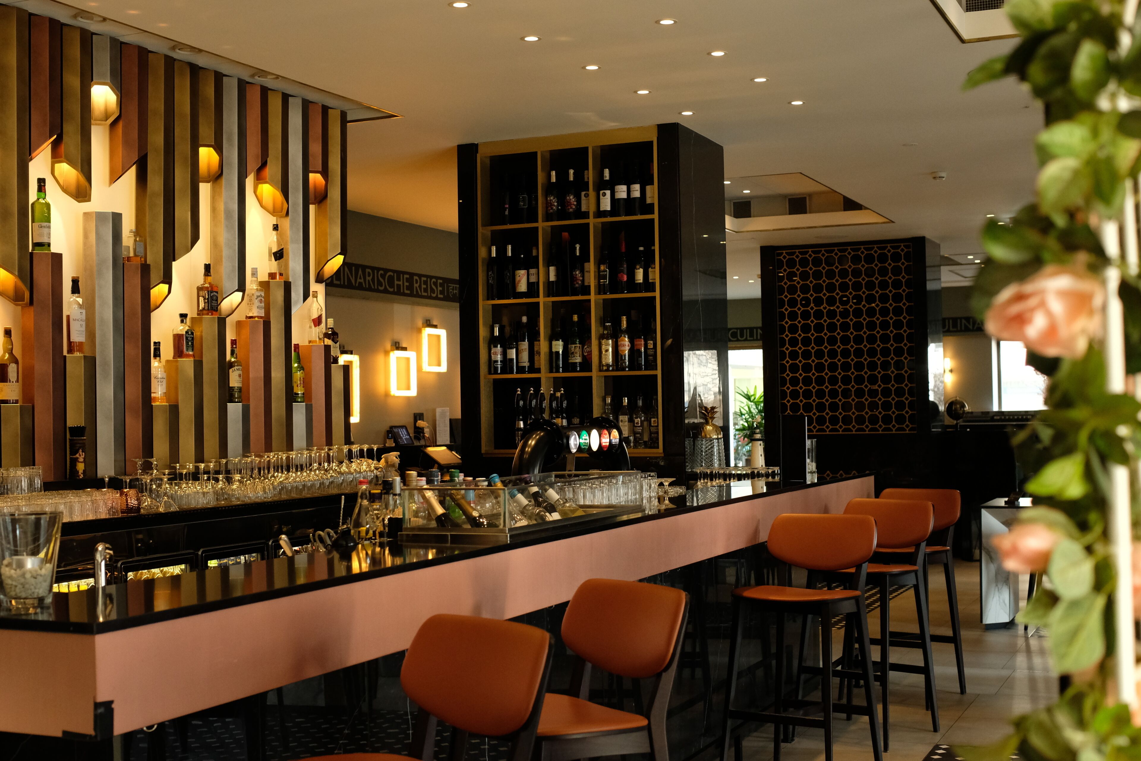 Eine Bar mit einer langen Theke, verschiedenen Sitzmöglichkeiten und einer Auswahl an Flaschen und Gläsern.