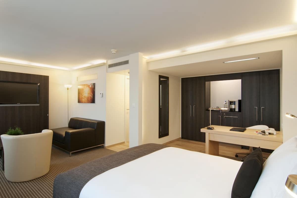 Ein modernes Hotelzimmer mit einem großen Bett, einem Schreibtisch mit Stuhl, einer Couch, einem Flachbildfernseher und einem Kleiderschrank.