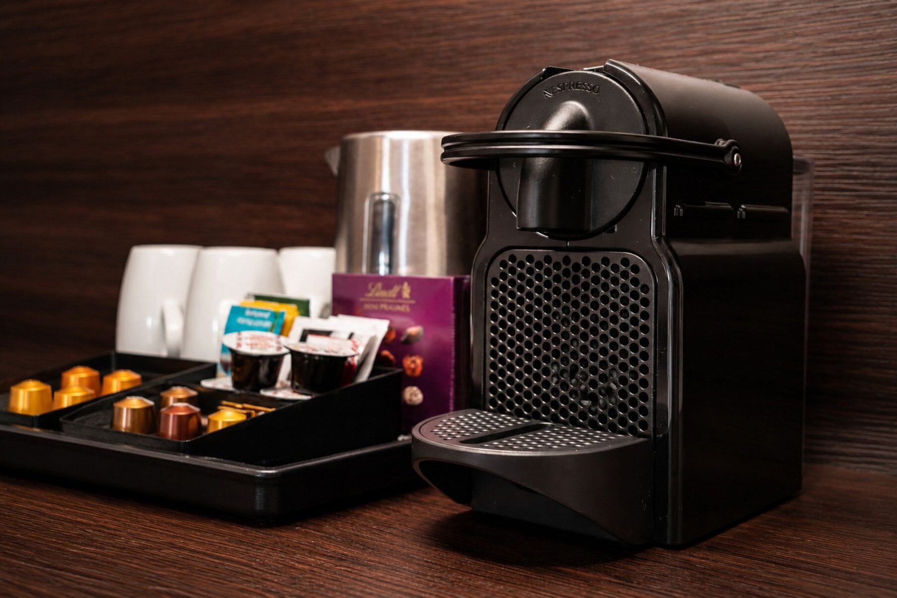 Een koffieapparaat met een lekbak, koffiekapsules en een waterreservoir op een houten oppervlak.