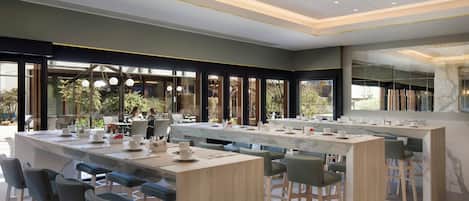 Un comedor moderno con una barra alargada, diversas opciones de asiento y grandes ventanales con vistas al exterior.