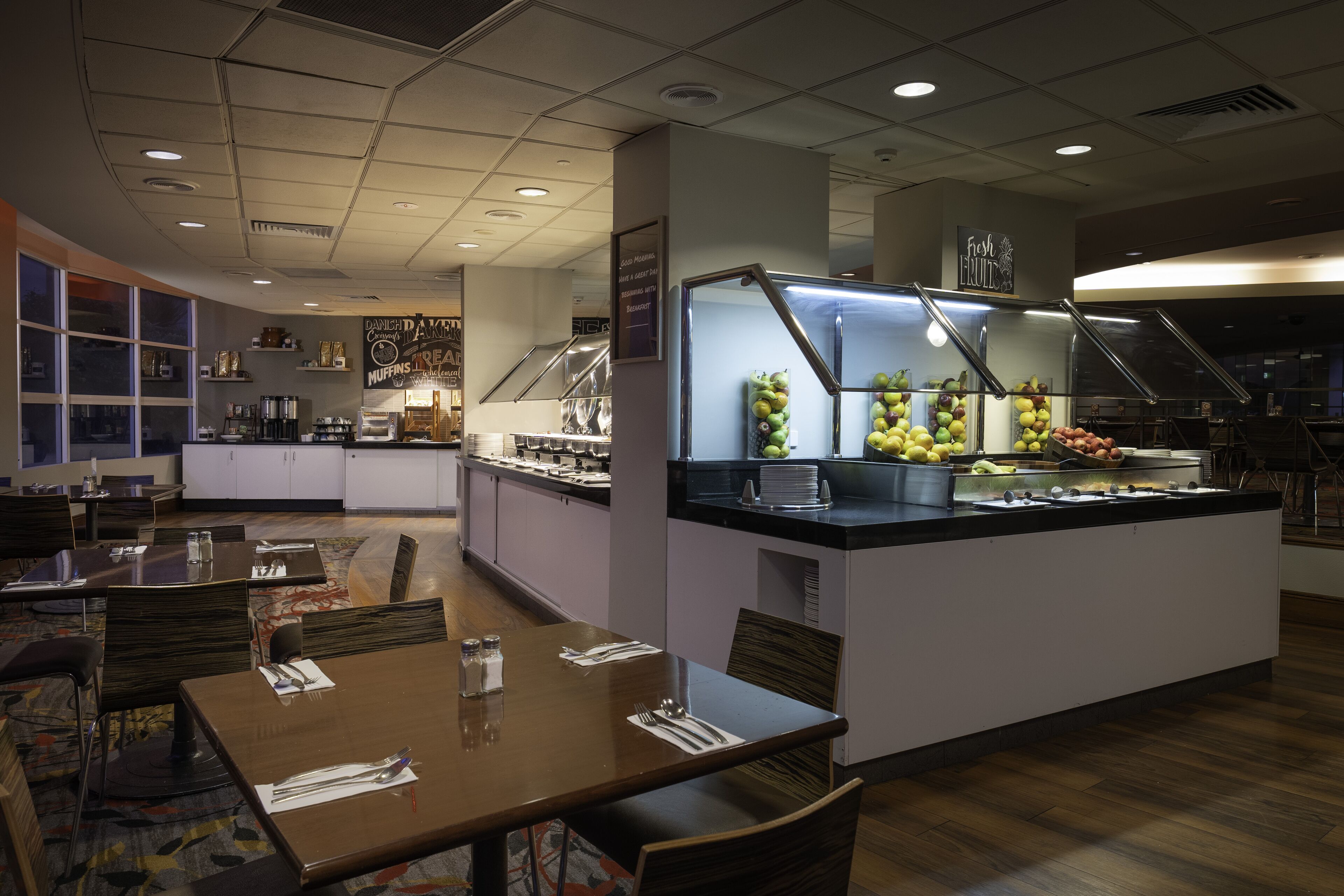 A buffet area with a central island displaying fruits and vegetables, surrounded by dining tables and chairs.
