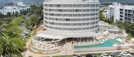 A multi-story hotel with a curved facade, a swimming pool, and a landscaped patio area.